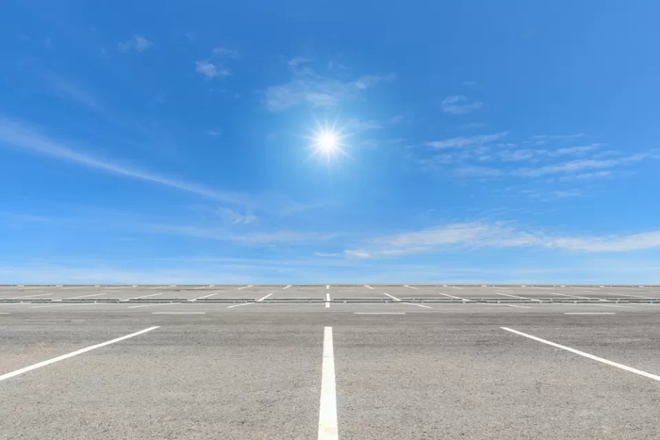 Vast, empty parking lot with blue sky and bright sun in background